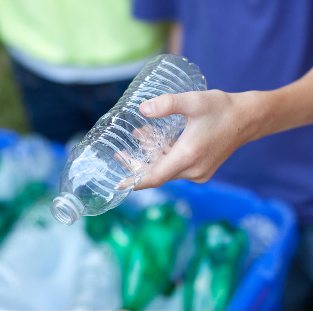 Caucasian boy and girl putting clear and green bottles and metal cans in recycling blue bin outside in yard