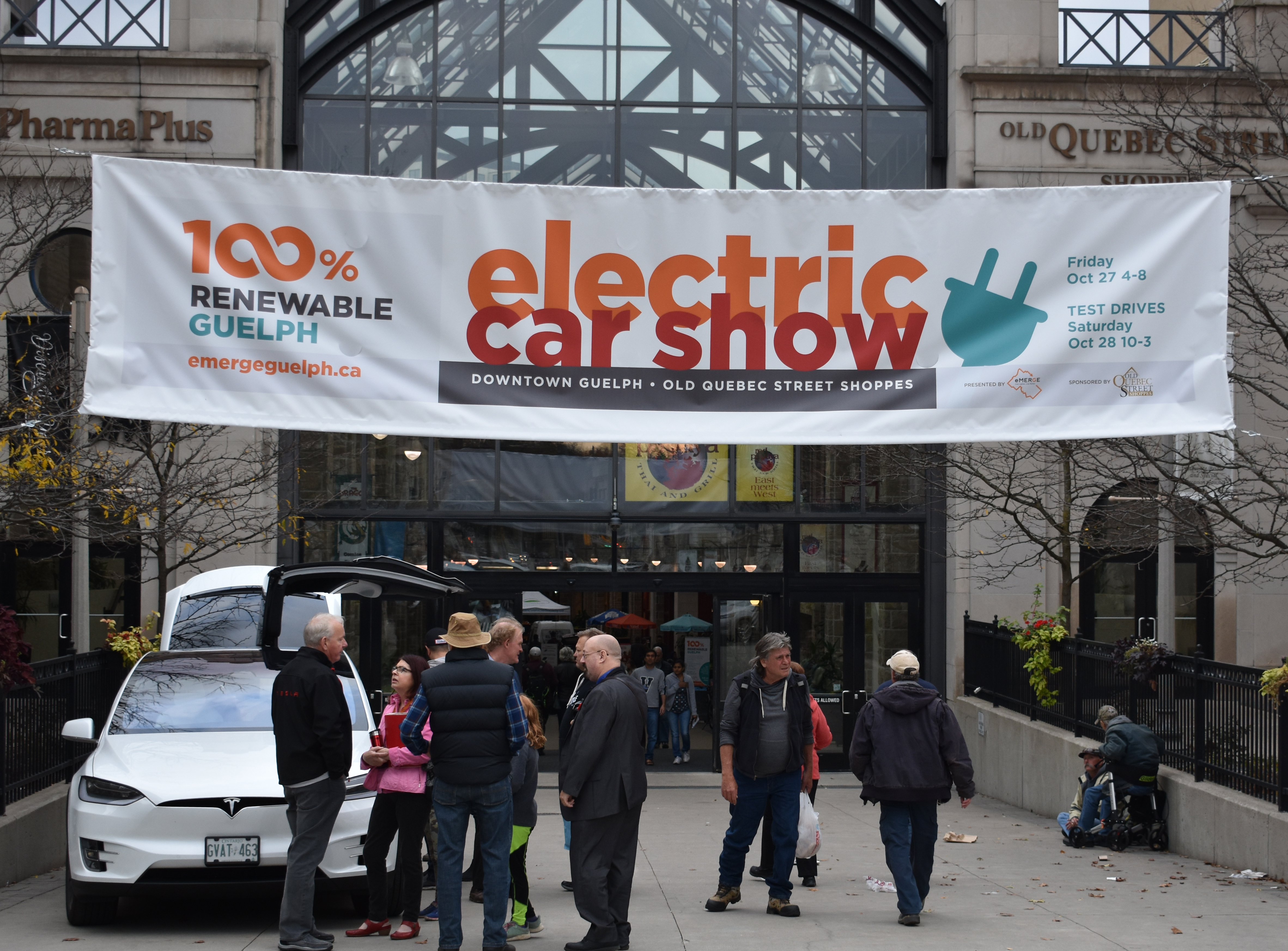 The front of Old Quebec Street Shoppes, Guelph, with a large electric car show banner and a crowd of people